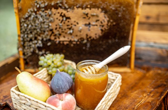 Composition of sweet fruits and jar with honey on the beehive with honeycomb on the background